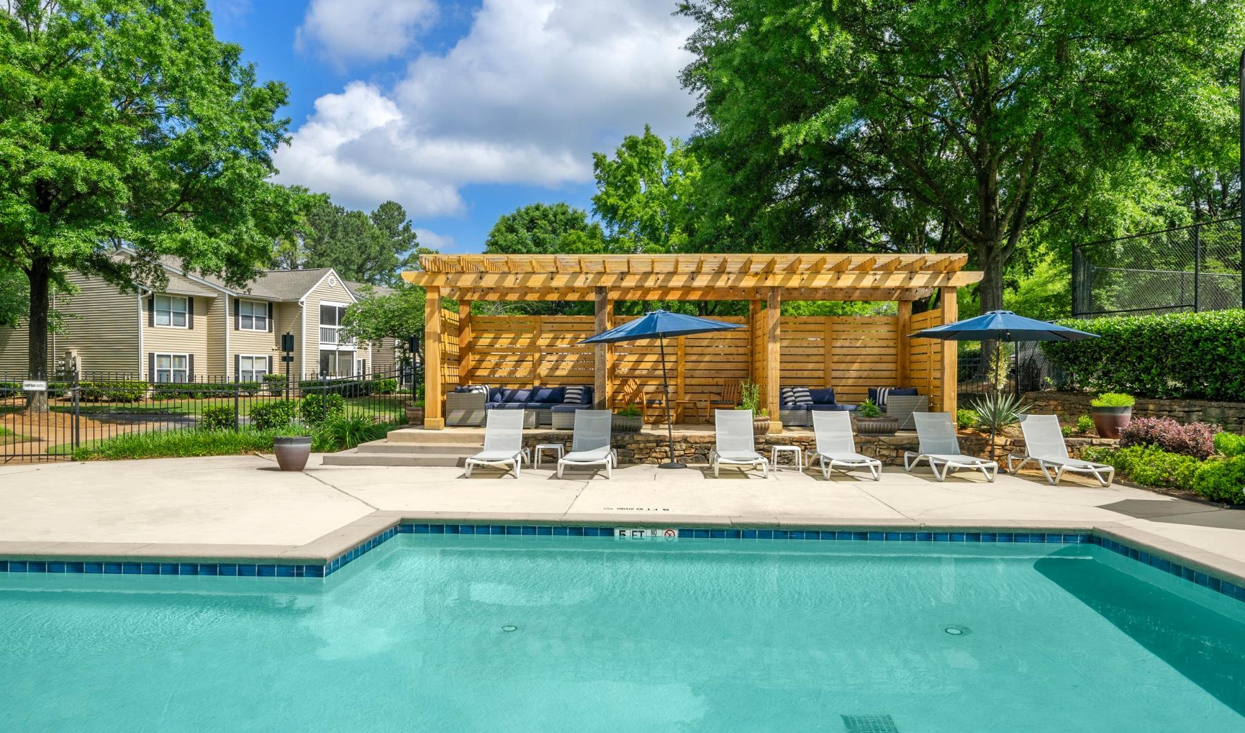 a pool with chairs and umbrellas by a house